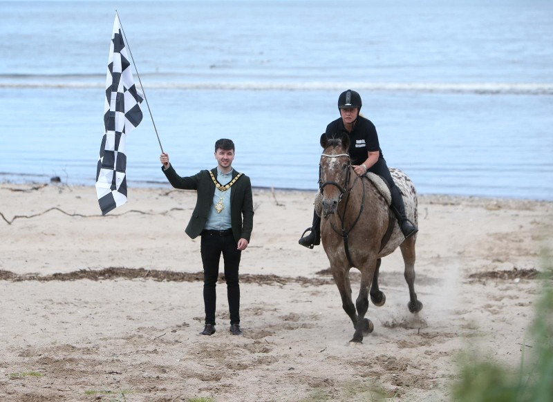 Ould Lammas Fair Chief Horse Steward Melissa Lemon prepares for Ballycastle Beach Races alongside the Mayor of Causeway Coast and Glens Borough Council Councillor Sean Bateson with the iconic Fairhead cliff edge in the background. The races will take place on Saturday 24th August as part of the Ould Lammas Fair programme of events, promising an evening of not-to-be-missed fun and entertainment.