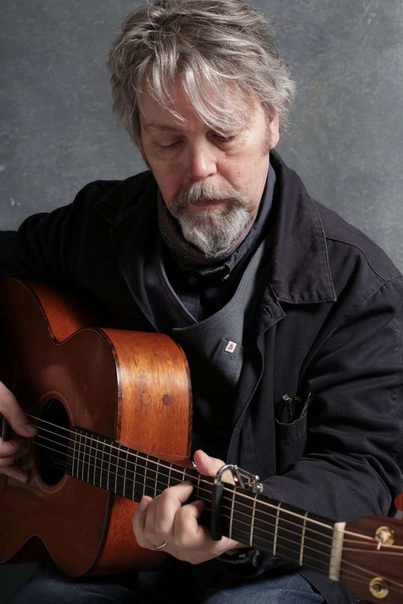 Anthony Toner pictured wearing dark clothing, sitting down playing a guitar.