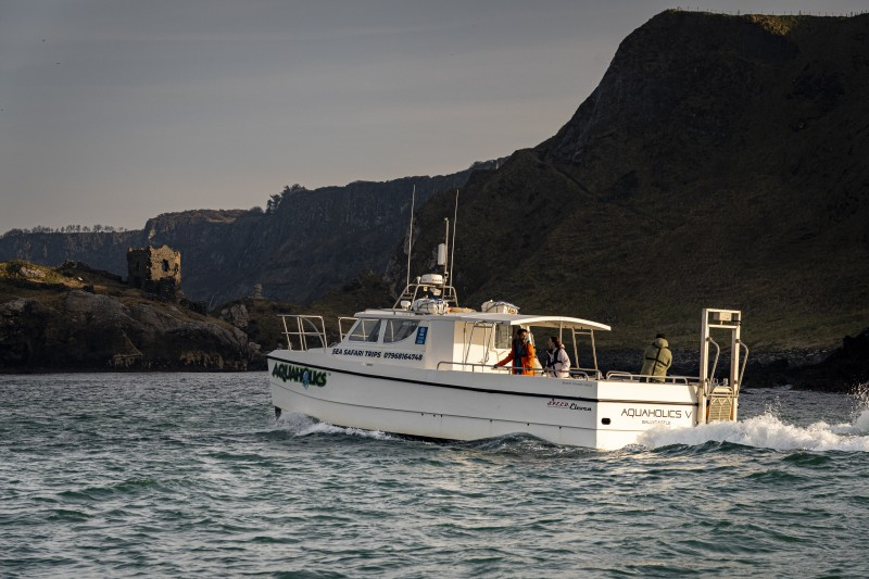 Aquaholics Sea Safari taking a tour of the Causeway Coast from the water, with cliffs and ruins in the background. Credit: Tourism Northern Ireland.