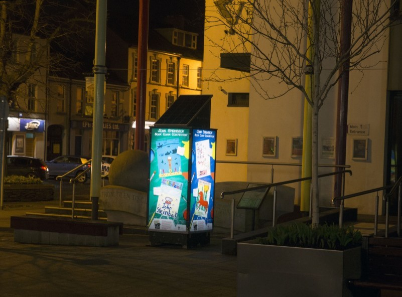 One of the light boxes on display at night in Drumceatt Square featuring some of the colourful book cover designs.