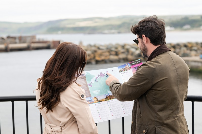 A man and woman at Ballycastle Harbour, reading a map of the local tourism destinations to visit.