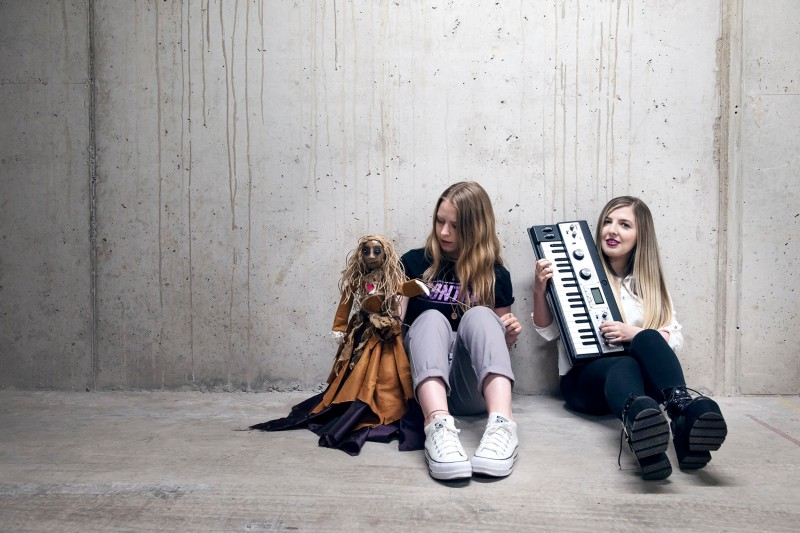 Vokxen – two girls sitting on the floor. One with a puppet and the other holding a keyboard.
