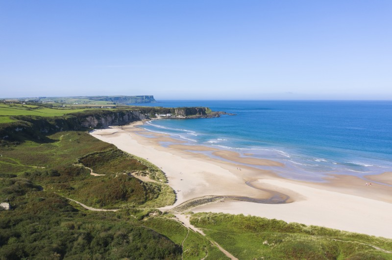The long stretch of sand at White Park Bay, with a blue sea and Portbradden in the distance. Credit: Chris Hill Photographic for Tourism Ireland.
